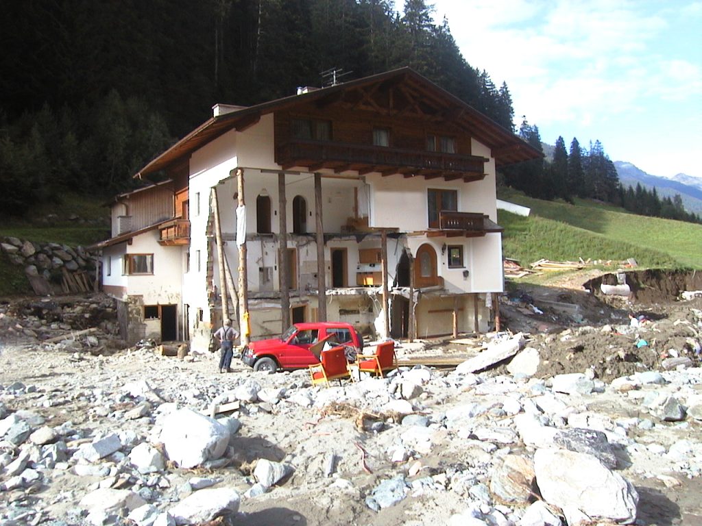 Von Mure zerstörtes Haus mit rotem Auto